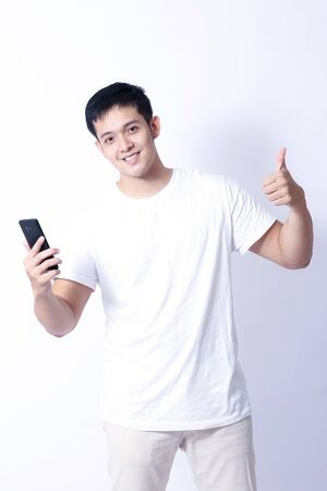 A Portrait of young asian wearing a Green t-shirt and white jeans showing gesture sign or devicesの写真素材