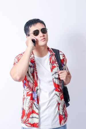 A Portrait of young tourist asian man wearing floral shirt and showing gesture sign or laptop, Smartphone, camera  and wallet stand in isolated backgroundの写真素材