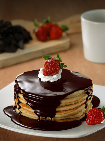 Stack of pancakes with chocolate syrup, whipped cream and strawberries.の写真素材