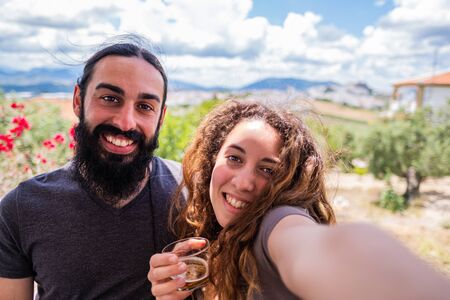 Couple of blonde curly hair woman and long black hair and beard man taking a selfie on a terrace with the town in the backgroundの写真素材