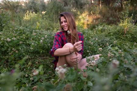 Young woman sitting in the grass smelling a flower and surrounded by flowers and tall grass