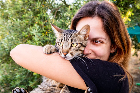 Close portrait of young brown-eyed latin woman hugging her green-eyed tabby cat