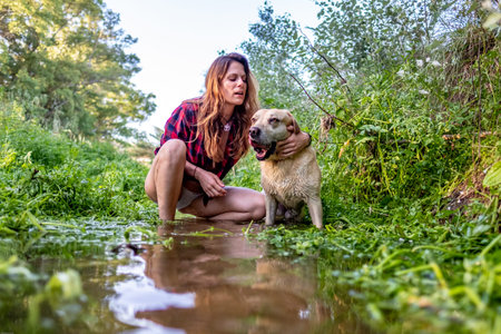 Young woman taking a walk with her dog in the river surrounded by tall green grasses