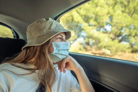 Little girl in hat and mask looking thoughtfully out of car window