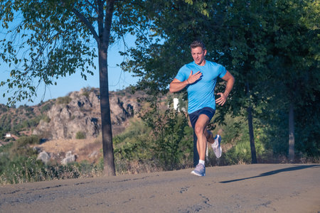 Young man in blue shirt and young woman in purple shirt running through a park with trees in the...