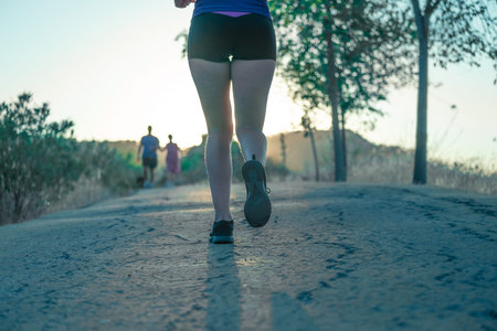 Backlit photo of young woman's legs running through the park in the afternoonの写真素材