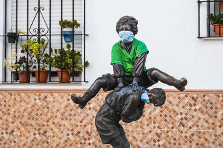 Bronze statues of two children playing in the street jumping on top of each other wearing face masksの写真素材