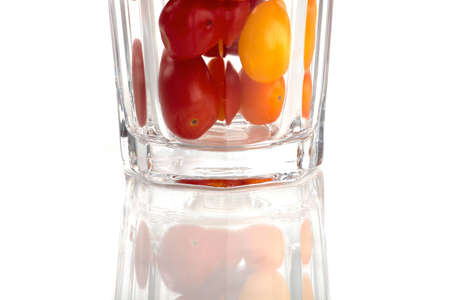 A glass filled with colorful small organic tomatoes in front of white backgroundの写真素材