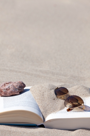 Sunglasses with brown tinted lenses lies on an opened book on the beachの写真素材