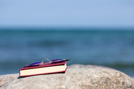 Closed Book with dark tinted sun glasses lies on a rock on the beachの写真素材