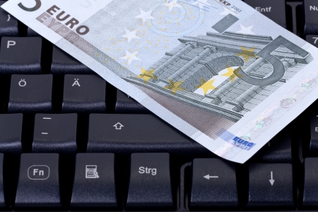 Detail view of a black computer keyboard with a five euro banknote on the topの写真素材