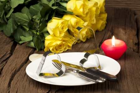 Romantic arrangement of al plate with metal heart shapes, a bouquet of yellow roses and a candle on a old wooden boardの写真素材