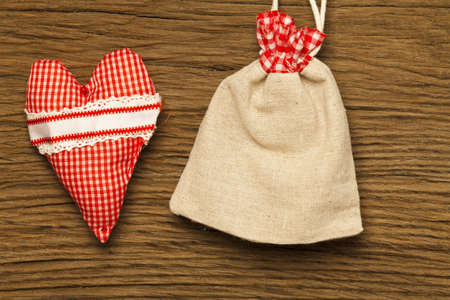 A red and white checked fabric cushion and a small jute bag before wood backgroundの写真素材