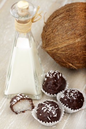 With bittersweet chocolate covered coconut milk rice truffles, a coconut and a bottle of coconut cream on a wooden traの写真素材