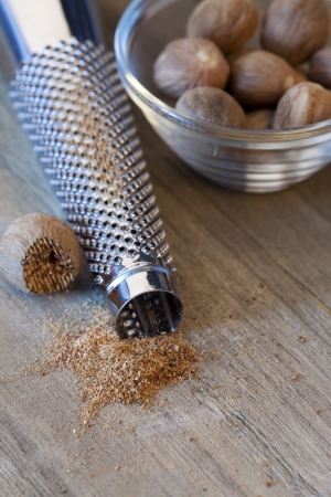 Nutmeg in a bowl next to a grater and nutmeg powderの写真素材