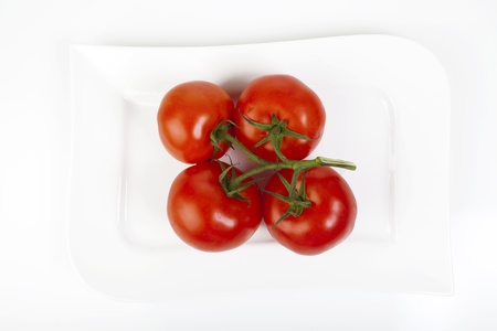 Four whole trusses of tomatoes on a white porcelain plateの写真素材