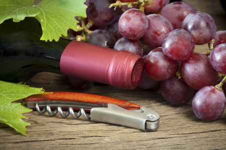 Ripe red grapes with vine leaves are by a wine bottle and corkscrew on a wooden backgroundの写真素材