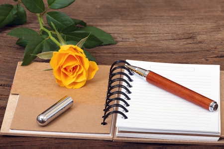 Note Pad opened with writable page, a Pen and a Orange Rose on old wooden Backgroundの写真素材