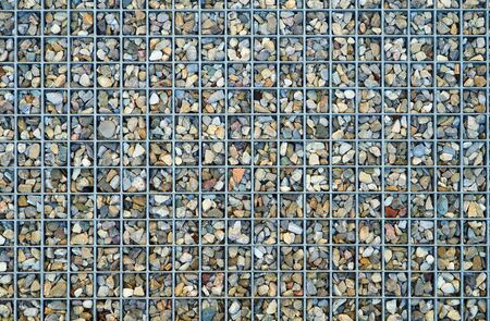 Small pebbles lie in the interstices of a metal gridの写真素材