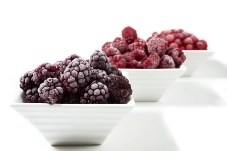 Three small porcelain dishes with frozen raspberries, currants and blackberries on white backgroundの写真素材