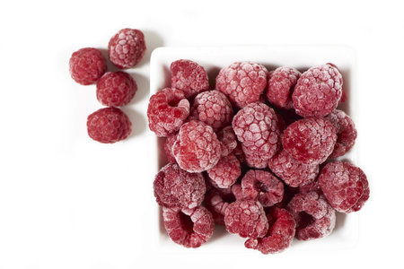 Close up of some frozen raspberries in a white porcelain dish on a white background