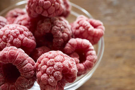 Macro shot of some frozen raspberries in a glass bowl on a wooden tableの写真素材