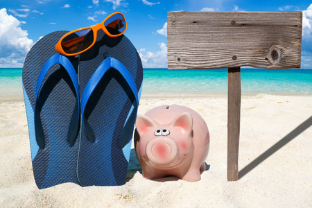 Pink piggy bank, Sunglasses, blue Flip Flops and a wooden Signboard on the Beachの写真素材