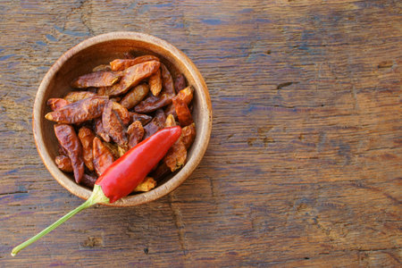 One whole chili pod on a bowl with dried chili on an old rustic wooden table with copy spaceの写真素材