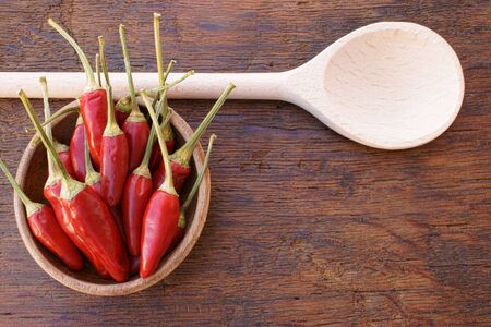 Red Chili pepper pods in a bowl and wooden cooking spoon on an old rustic wooden table with copy spaceの写真素材