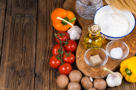 Fresh ingredients for a pizza dough and pizza topping on a wooden board made of olive wood with copy space in the left part of the pictureの写真素材
