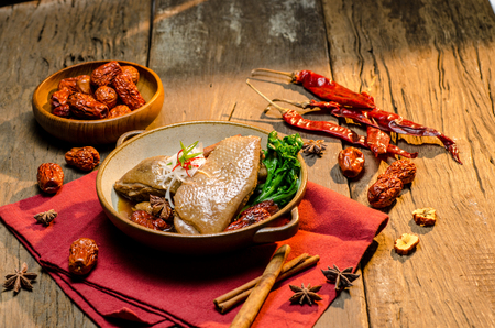 The chinese stewed duck with steamed ingredients in tile bowl on wooden tableの写真素材