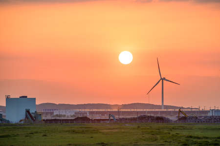 Wind turbines and factories illuminated by the sunsetの写真素材