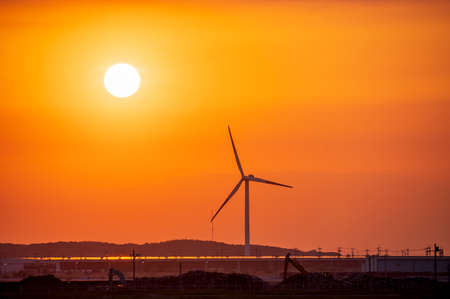 Wind turbines and factories illuminated by the sunsetの写真素材