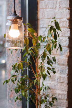 Vintage hand made style lamp on the restaurant window near the plant. Cozy lighting decor for cafe