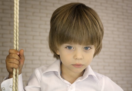 Blue-eyed boy in a white shirt with ropeの写真素材