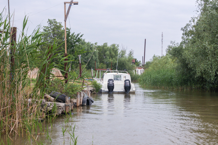 Vilkovo, Ukraine - May, 26, 2018: Canal along the street, reeds and white motor boatのeditorial素材
