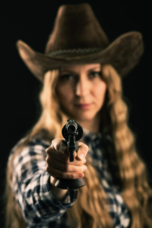 Lovely blonde posing in studio with a cowboy hat and a gun