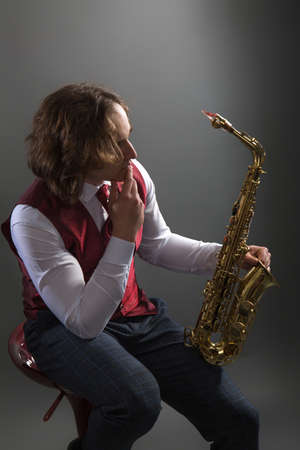 Young musician in a red vest sits and holds a saxophoneの写真素材