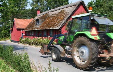 tractor drive past cottage, green agriculture machine and red farmの写真素材