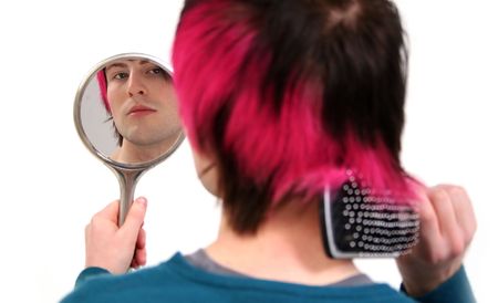 brush hair and grooming whilst looking in mirror. young fashionable teenager or adult with black and pink hairの写真素材