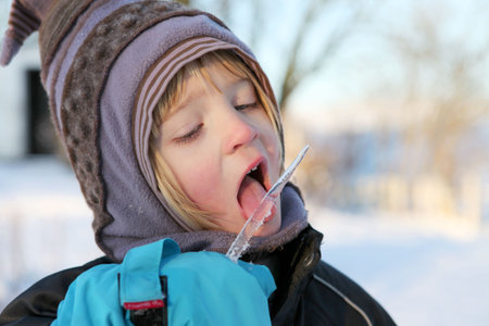 Child taste or licking icicle on winter day. boy with hat lick frosty ice