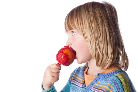 child eating toffee apple or taffy apple isolated on white. kid with sweet seasonal candy fruit snackの写真素材