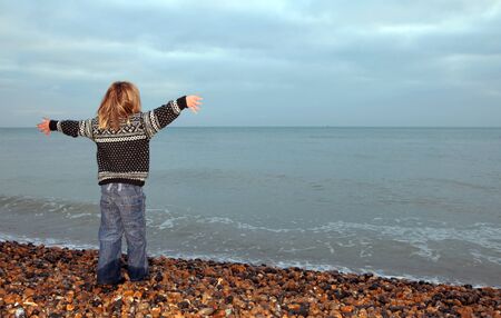 child at seaside out of season. boy looking at ocean on cold dayの写真素材