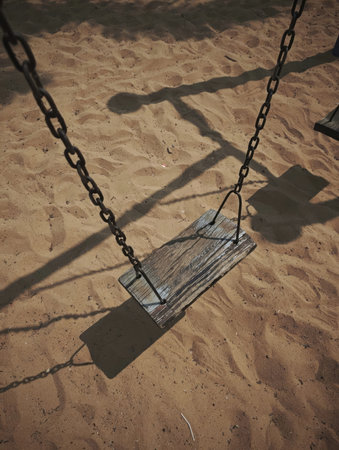 Wooden swing on the beach with shadow of a swing on the sandの写真素材