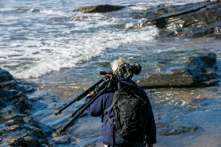 A professional photographer waits with his camera gear and tripod  for the retreating tide at...