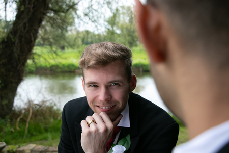 Gay couple of grooms pose for photographs by a lake on their wedding dayの写真素材