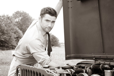 Handsome American WWII GI Army officer in uniform and rolled up sleeves next to broken car
