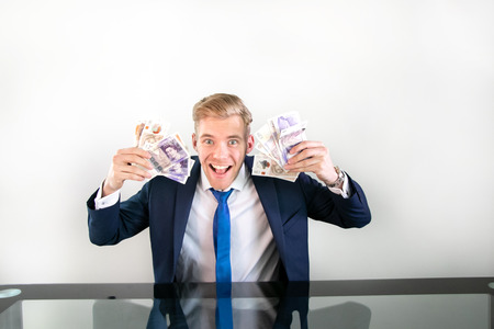 Happy man in suit holding wads of money of pound sterling banknotes in his handsの写真素材