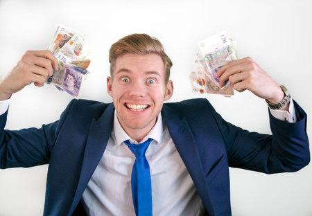Happy man in suit holding wads of money of pound sterling banknotes in his hands