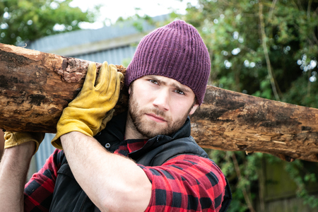 Handsome male lumberjack carries wood log on his shoulderの写真素材